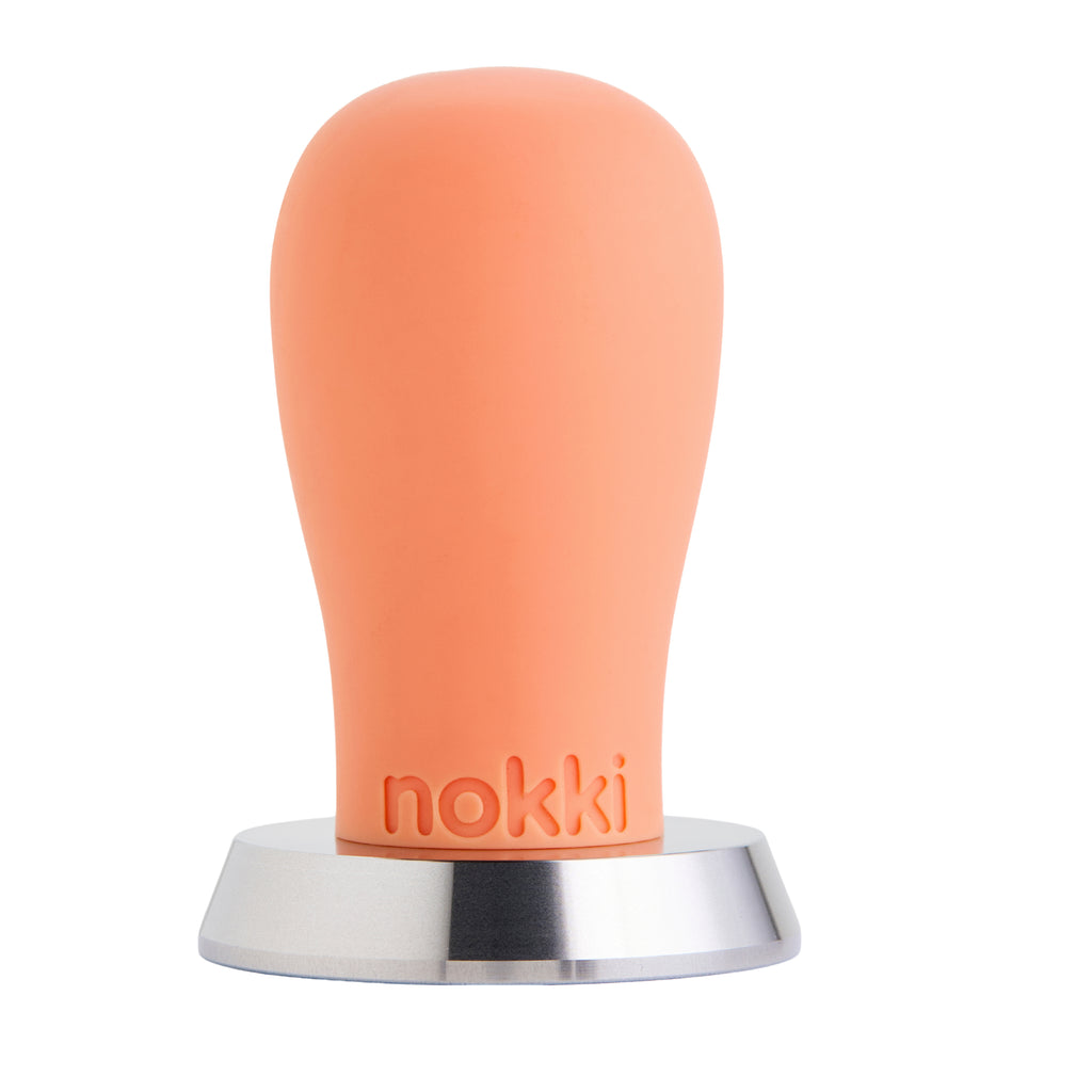 A Nokki 51mm coffee tamper with a matte orange silicone handle and a machined 316 stainless steel base, shown on a solid white background.
